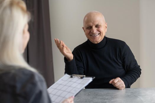 Portrait of female psychiatrist interviewing senior man during therapy session, copy space.