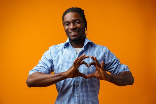 Young black man doing a heart sign over yellow background, close up