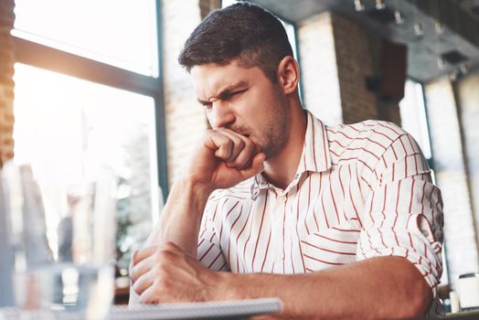Looks like something wrong. Adult man sits in cafe at daytime and read some hard explained information.