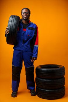 African american car service worker with car tyre against yellow background, close up