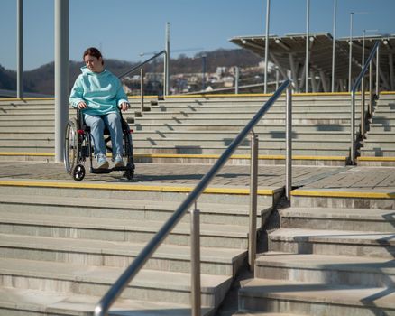 A caucasian woman in a wheelchair cannot go down stairs without a ramp. Hard to access environment