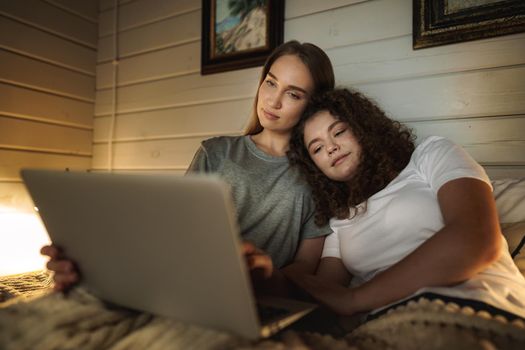 Two beautiful women lying in bed and watching movies on laptop at home