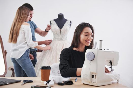 Nice atmosphere. Female fashion designer works on the new clothes in the workshop with group of people behind.