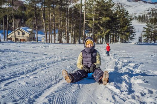 Happy woman having fun during rolling down the mountain slope on sled. Winter sports with snow. People riding a sledge.