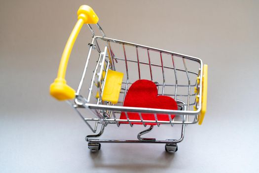 Shopping basket on a gray background with a bright red heart. Close-up