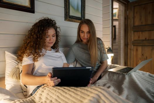 Two beautiful women lying in bed, holding and watching laptop