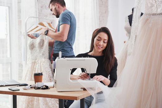 It's important to love your job. Female fashion designer works on the new clothes in the workshop with man behind.