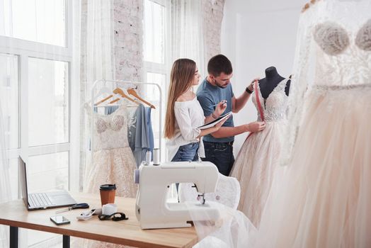 Two people measures breast place of the cloth. The process of fitting the dress in the studio of hand crafted clothes.