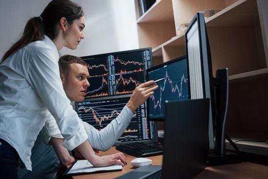 Team of stockbrokers are having a conversation in a office with multiple display screens.