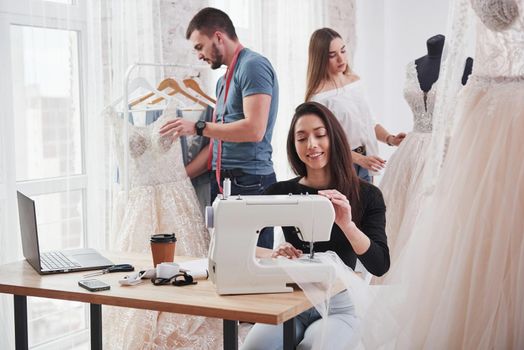 Job is on progress. Female fashion designer works on the new clothes in the workshop with group of people behind.