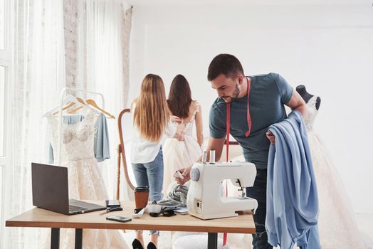 Guy holds cloth and takes some instruments for work. The process of fitting the dress in the studio of hand crafted clothes.