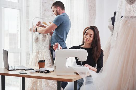 Employee behind. Female fashion designer works on the new clothes in the workshop with man behind.