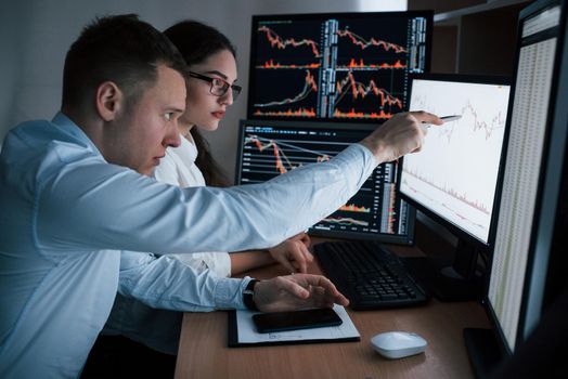 Planning the business project. Team of stockbrokers are having a conversation in a office with multiple display screens.