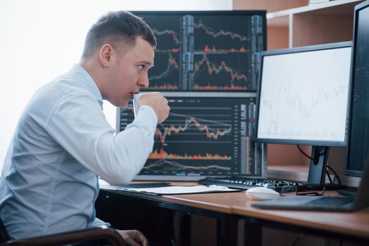 Drinks some coffee to stay concentrated. Man working online in the office with multiple computer screens in index charts.