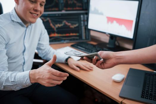 Happy guy receive his money. Day of salary in the modern office with screens with graphs on them.