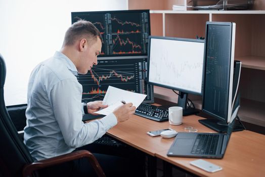 Reading the report. Man working online in the office with multiple computer screens in index charts.