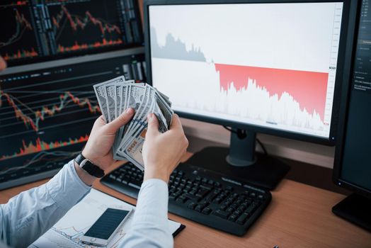Recounts money. Man working online in the office with multiple computer screens in index charts.