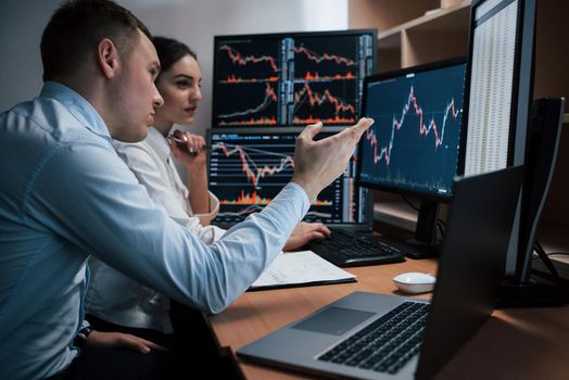 Team of stockbrokers are having a conversation in a office with multiple display screens.