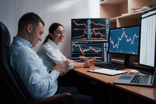 Team of stockbrokers are having a conversation in a office with multiple display screens.