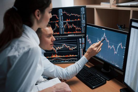 Team of stockbrokers are having a conversation in a office with multiple display screens.