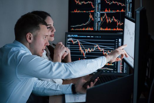 Team of stockbrokers are having a conversation in a office with multiple display screens.