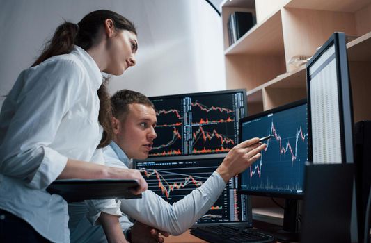 Team of stockbrokers are having a conversation in a office with multiple display screens.