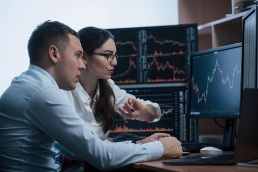 Team of stockbrokers are having a conversation in a office with multiple display screens.