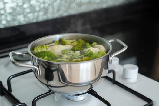 Green fresh broccoli is cooked in water in metal silver saucepan on gas white stove. Process of cooking vegetables.