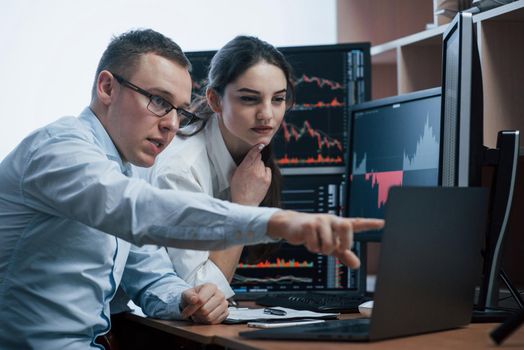 Team of stockbrokers are having a conversation in a office with multiple display screens.