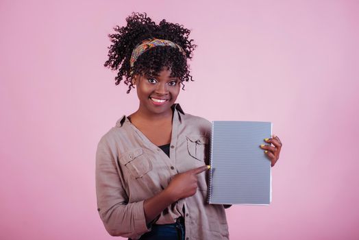 Holding notepad. Attractive afro american woman in casual clothes at pink background in the studio.