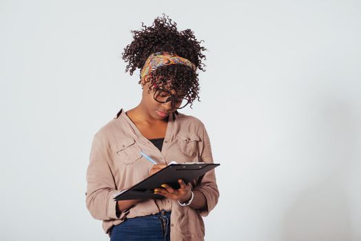 Student writes on the notepad. Beautiful afro american girl with curly hair in the studio with white background.