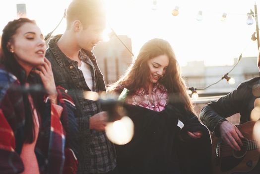 Playing some music. It's rooftop party. Group of friends have holidays at sunny autumn day.