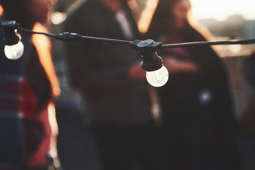 Close up view of light bulbs. Young people at background have rooftop party.