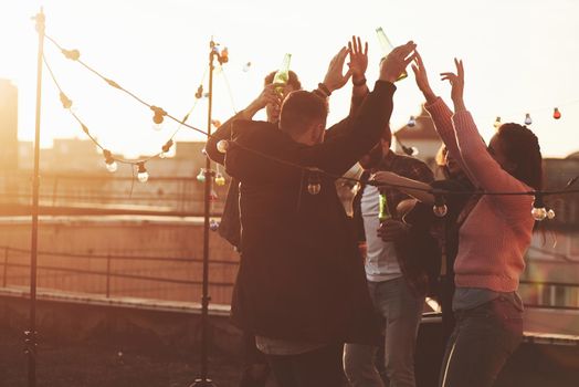 It's good weather. Holidays on the rooftop. Cheerful group of friends raised their hands up with alcohol.