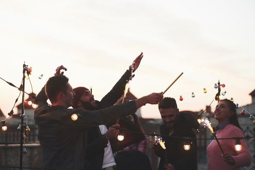 Right up into the air. Playing with sparklers on the rooftop. Group of young beautiful friends.