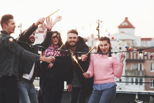 Girl showing gesture for the picture. Playing with sparklers on the rooftop. Group of young beautiful friends.