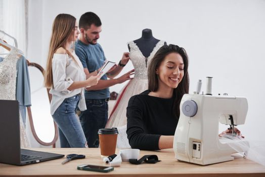 Making your dreams real. Female fashion designer works on the new clothes in the workshop with group of people behind.