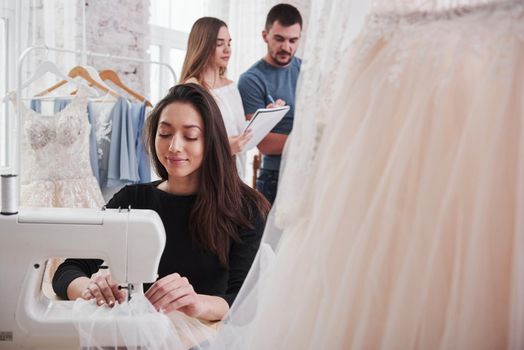 Employees makes calculations for an order behind. Female fashion designer works on the new clothes in the workshop.