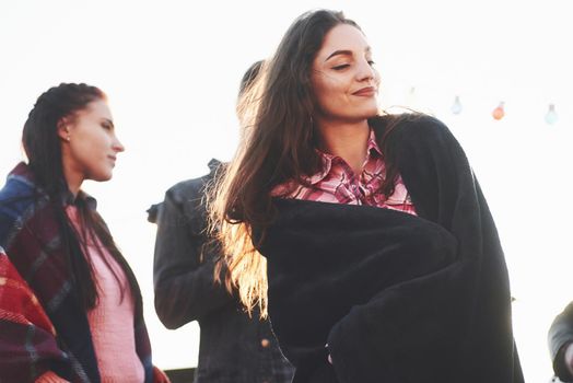 Girl is wearing warm clothes. It's rooftop party. Group of friends have holidays at sunny autumn day.