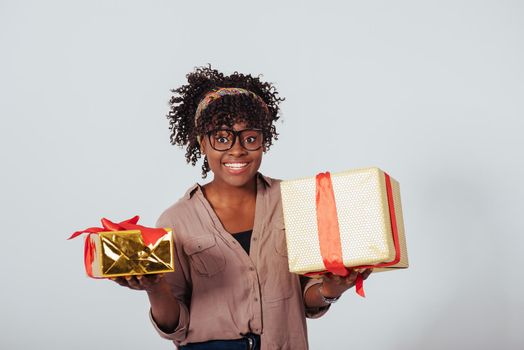 Holding two gift boxes and smiling. Holidays and celebration conception. Beautiful afro american girl with curly hair in the studio with white background.