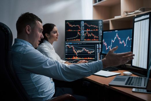 Team of stockbrokers are having a conversation in a office with multiple display screens.