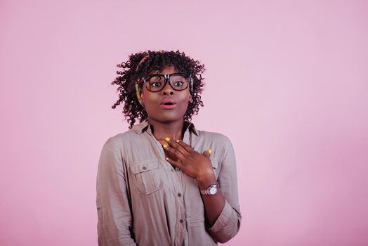 Shows shocking expression. Attractive afro american woman in casual clothes at pink background in the studio.