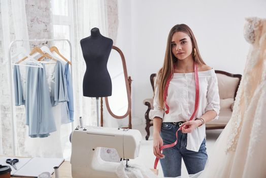 Looking into the camera. Female fashion designer works on the new clothes in the workshop.