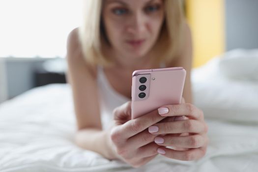 Woman lies in bed and looks at smartphone. Communication in chat and social networks concept