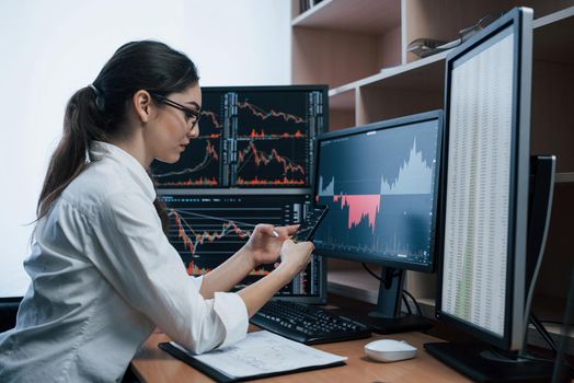 Gorgeous brunette. Woman working online in the office with multiple computer screens in index charts.