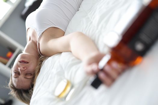 Drunk woman sleeping with bottle of alcohol in bed. Female alcoholism concept