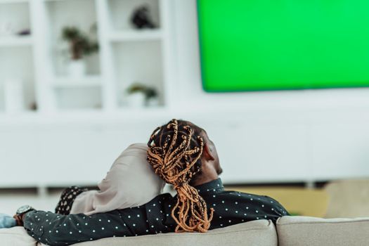 African Couple Sitting On Sofa Watching TV Together Chroma Green Screen Woman Wearing Islamic Hijab Clothes. High quality photo