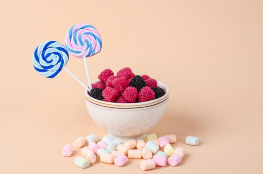 The Sweet gummy in cup and marshmallow on pastel orange background.
