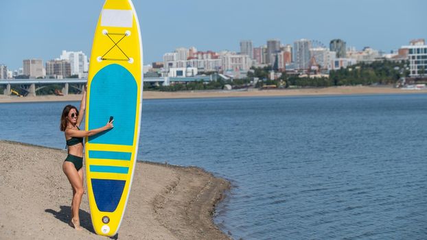 Caucasian woman walks along the beach and carries a sup board on the river in the city. Summer sport