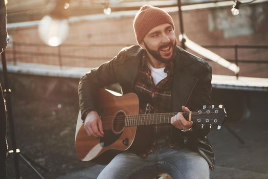 Bearded guy in cap playing and singing on the rooftop at nice autumn day.